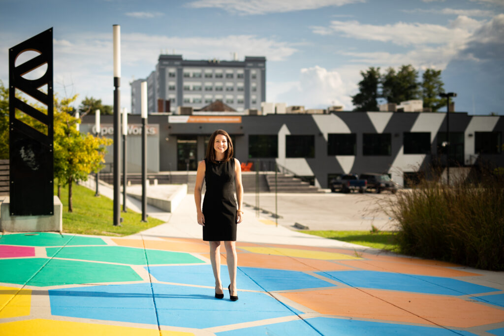Amanda standing in front of a building wearing a black dress. There are multicolored hexagons on the ground. 